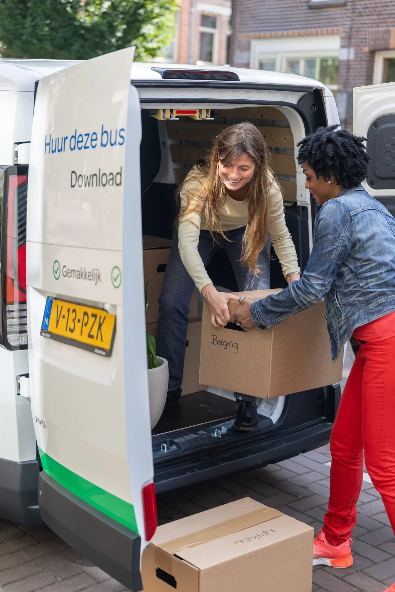 Vrouwen tillen verhuisdoos uit MyWheels bestelbus