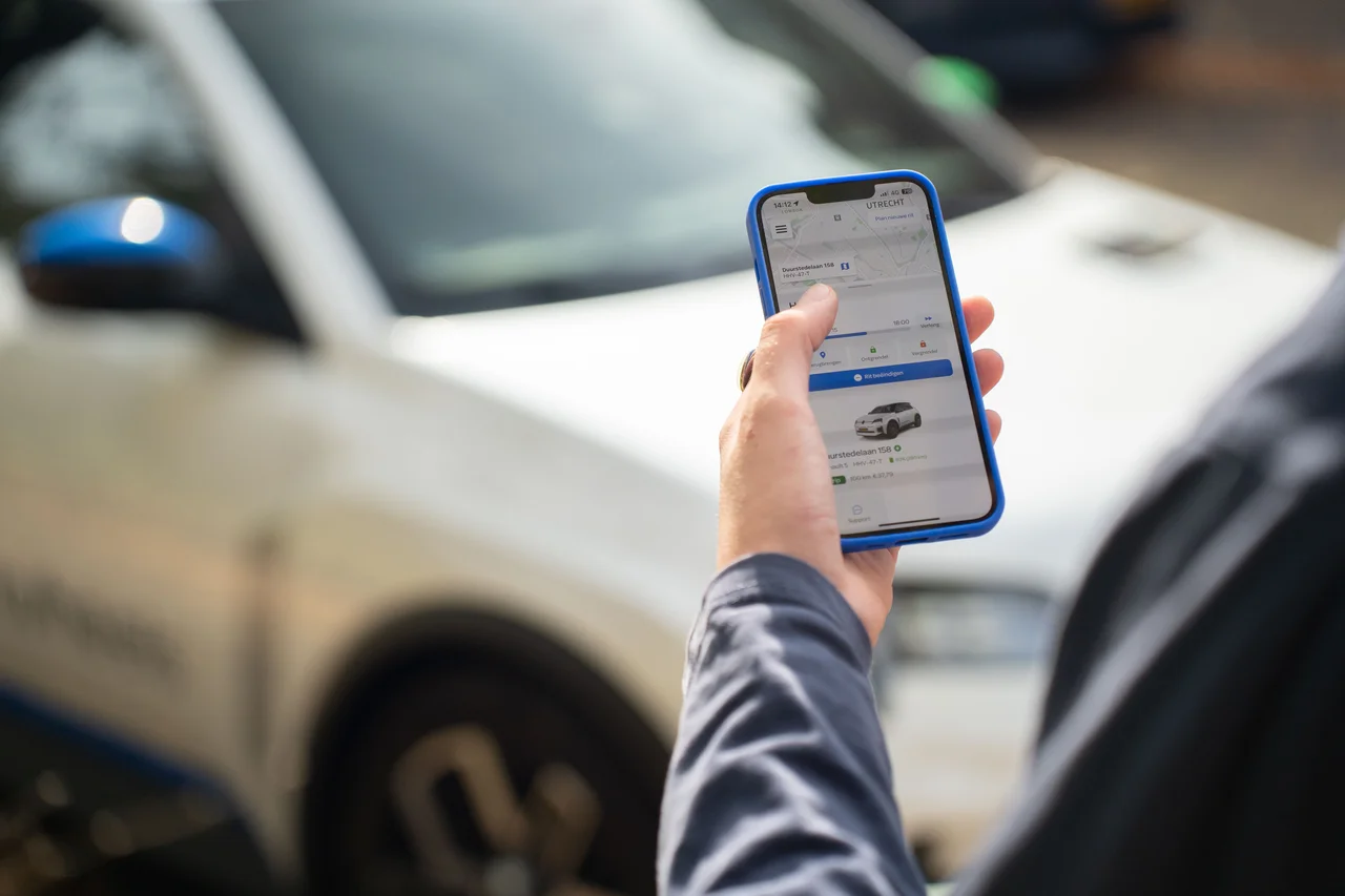 Hand met telefoon en MyWheels app voor autodelen